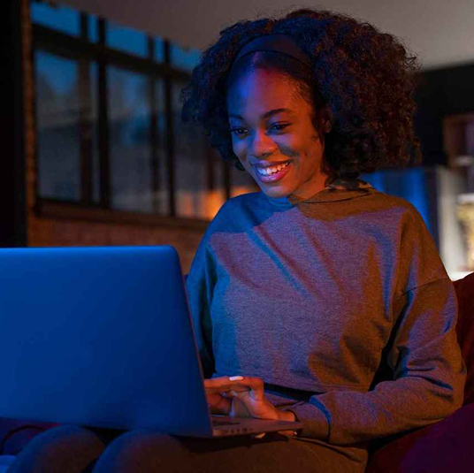 Smiling woman using a laptop, lit by warm room light